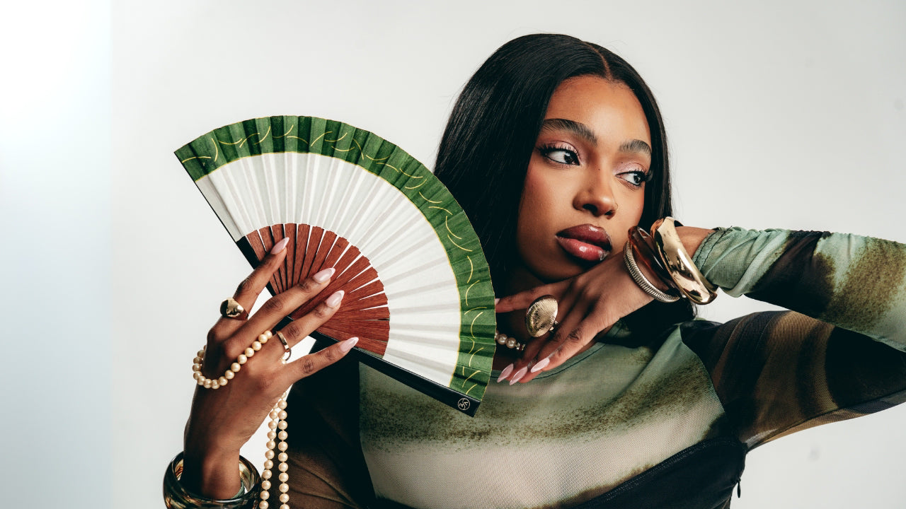 Woman holding a green and white fan against a plain background