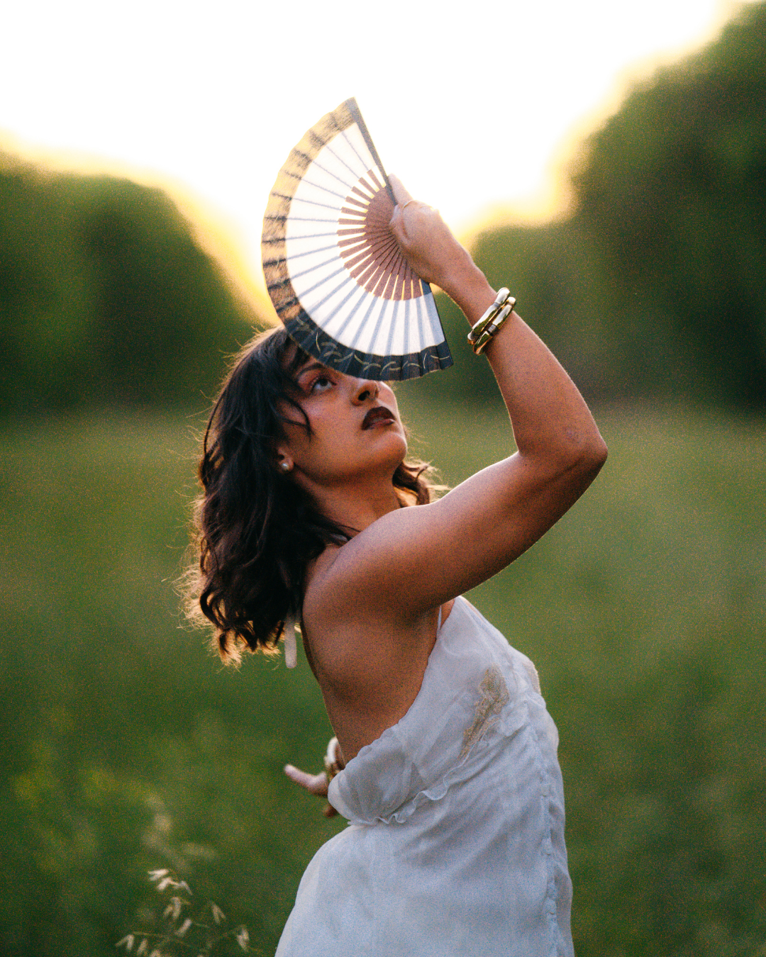 Woman holding a fan in a field with a blurred background